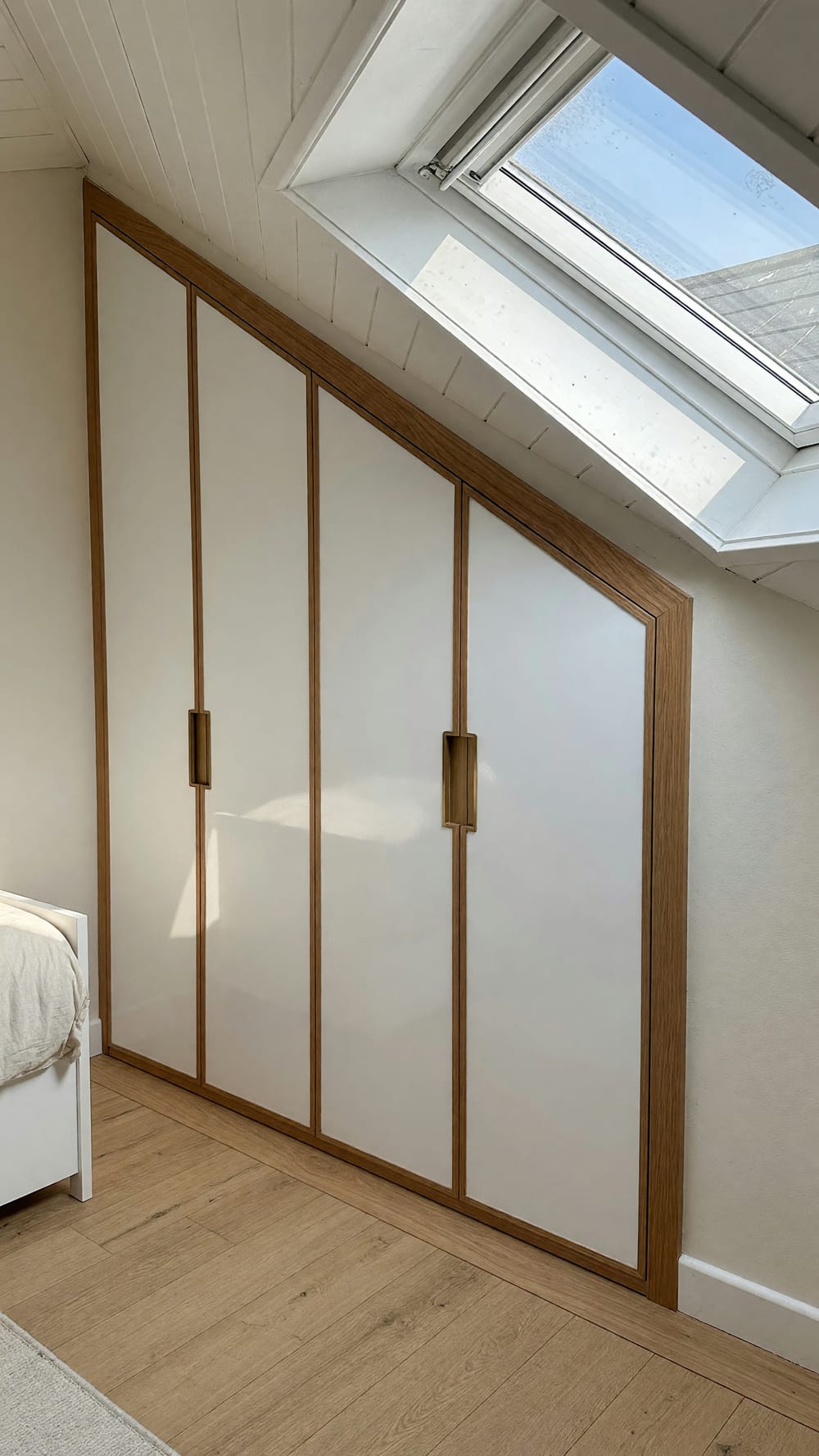 Einbauschrank in der Dachschräge: weiße Türen in einem Rahmen aus Eiche, darüber das Dachfenster